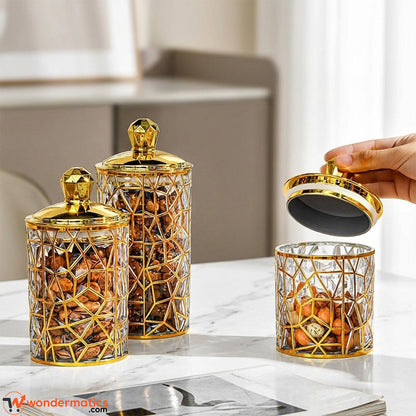 Three gold-patterned acrylic kitchen jars on a countertop holding sugar, tea, and coffee