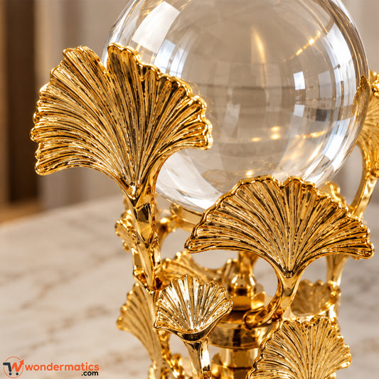 Close-up of ribbed golden metal ginkgo leaves supporting a crystal ball