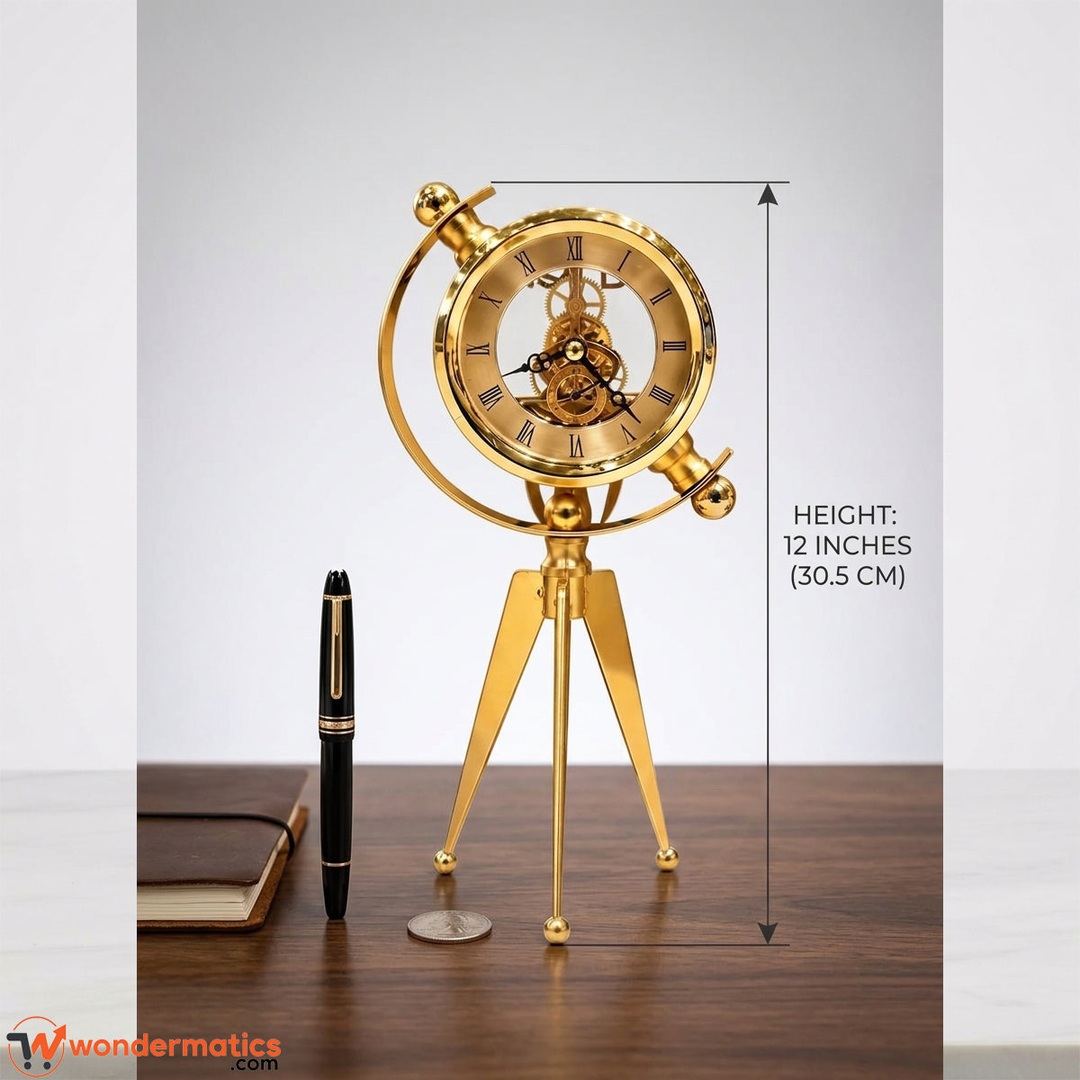 Gold-colored mechanical globe desk clock on a tripod stand, shown on a wooden table with a pen and notebook beside it, and a height measurement overlay indicating 12 inches (30.5 cm).