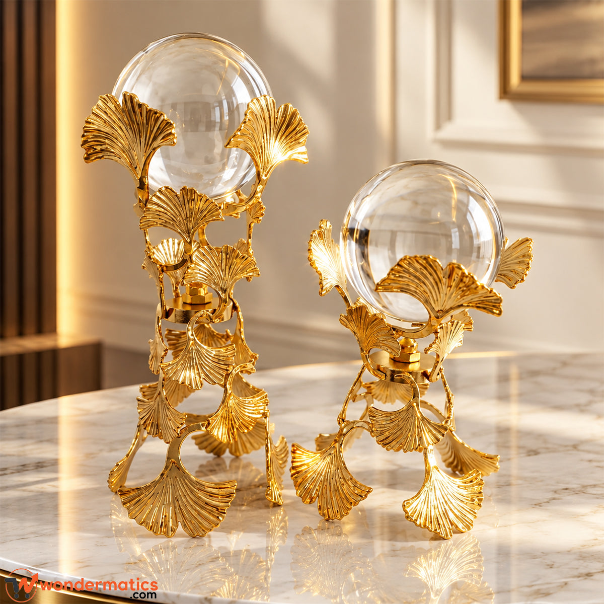 Two golden ginkgo leaf crystal ball showpieces in tall and short sizes on a white marble table