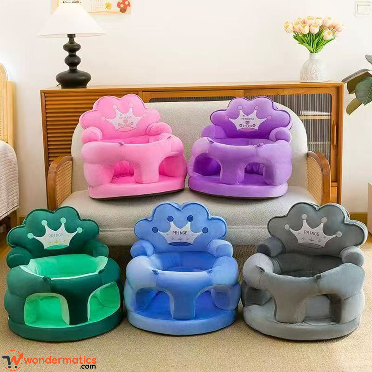 Four cloud-shaped prince and princes baby support plush chairs in pink, purple, green, and blue, along with one gray chair, arranged on and in front of a light-colored sofa in a living room setting.