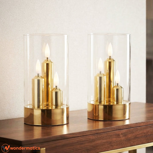 Two gold and clear glass candle holders with lit led flameless candles, displayed on a dark wooden table in a softly blurred indoor setting.