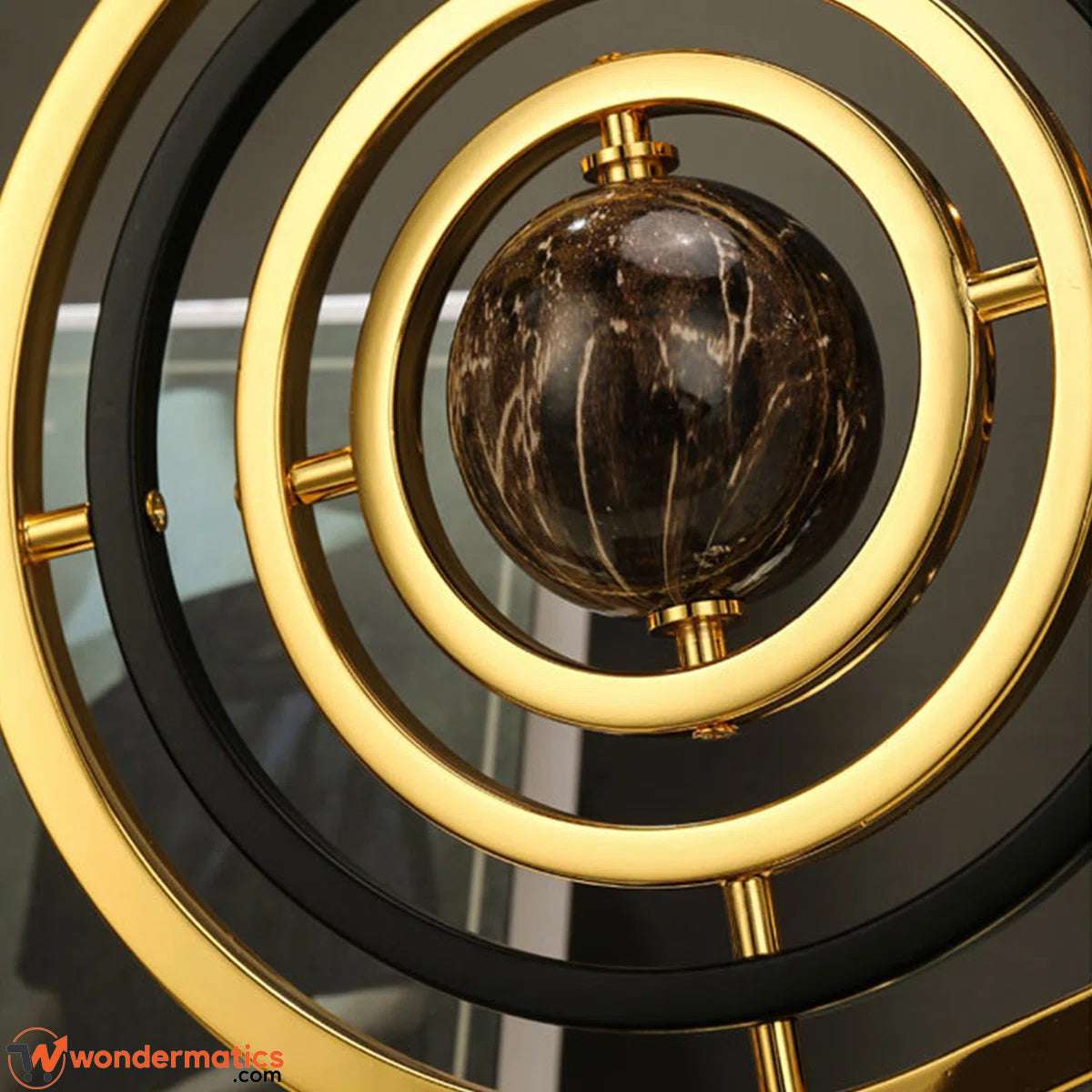 A close-up of a decorative metallic ring sculpture with concentric gold and black circular rings surrounding a polished dark brown marble sphere.
