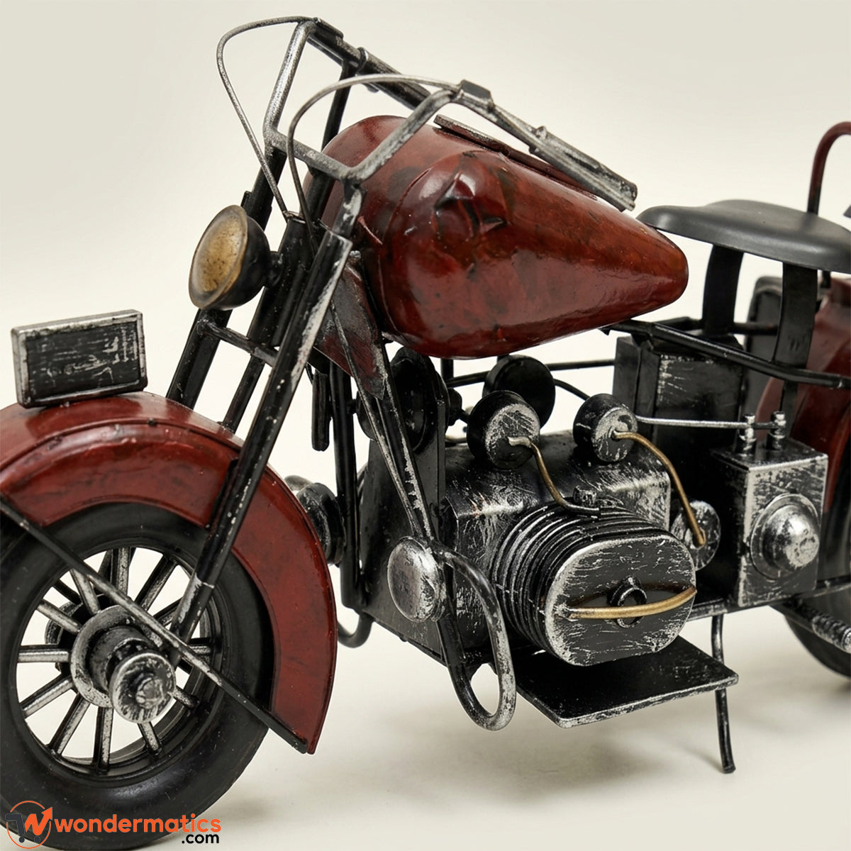 A vintage-style metal motorcycle sculpture or decorative model, shown in a close-up studio shot against a light neutral background. The motorcycle features a distressed reddish-brown fuel tank and fenders, black frame and seat, and weathered silver engine components.