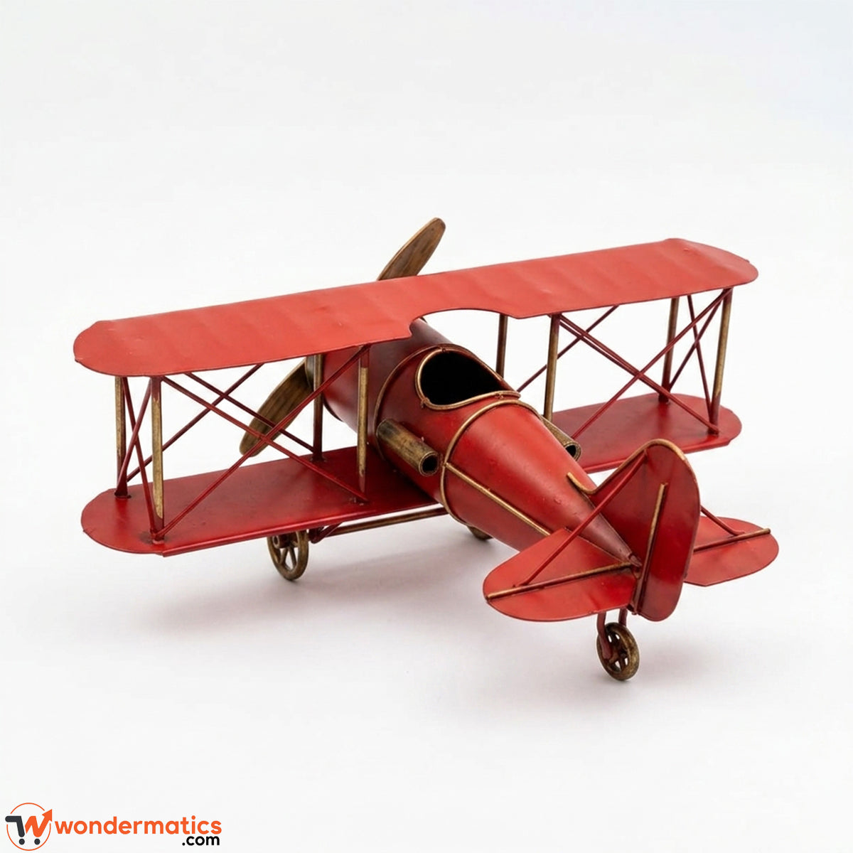 A red metal model of a vintage biplane with brass-colored wire framing and wheels, photographed on a clean white background.