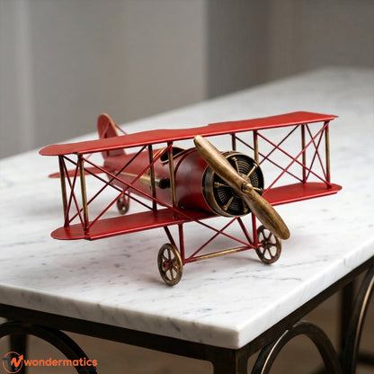 A red and gold metal model of a vintage biplane airplane displayed on a white marble table for home and office decor