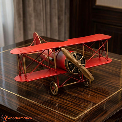 Red metal vintage biplane model displayed on a wooden desk